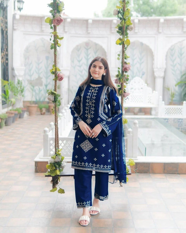 Woman in a blue embroidered outfit standing in a decorated outdoor setting.