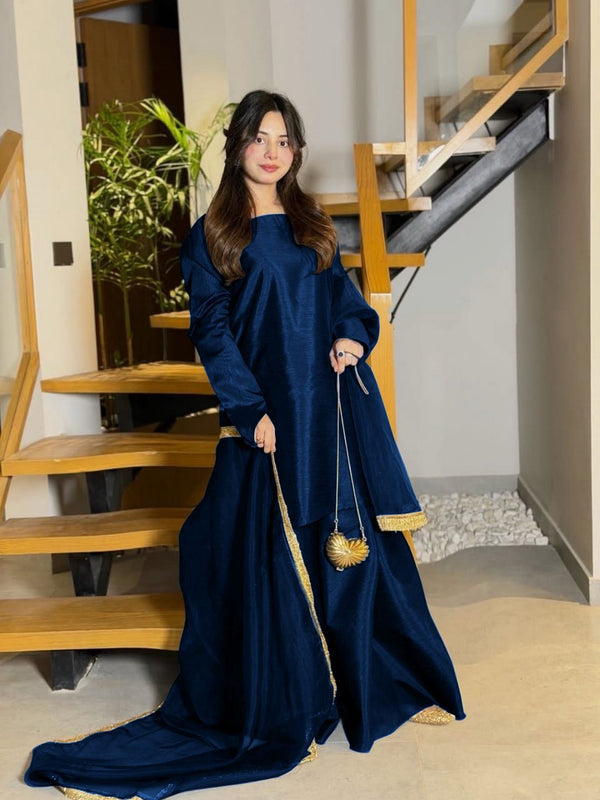 Woman in a long blue dress with gold trim standing in a home interior.