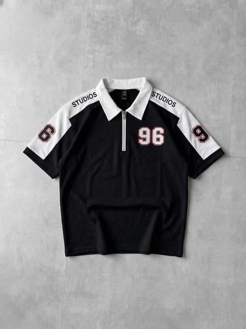 Black and white polo shirt with '96' and 'STUDIOS' text on a gray background