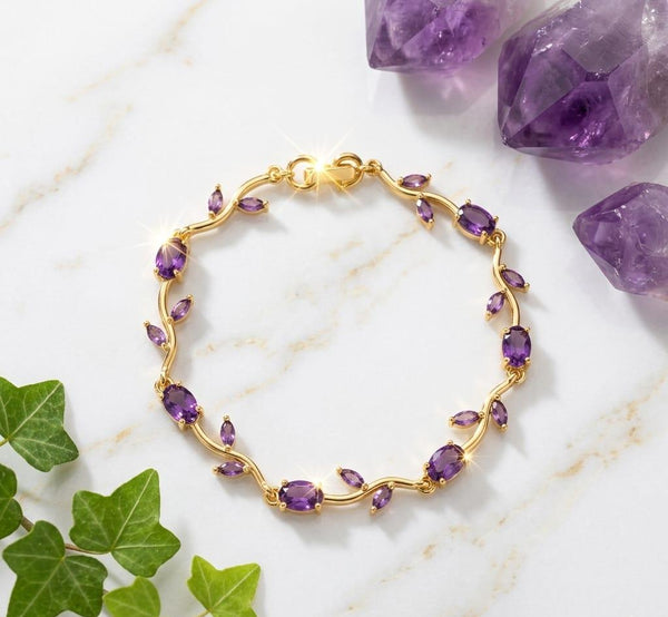 Gold bracelet with purple gemstones on a marble surface with amethysts and green leaves.